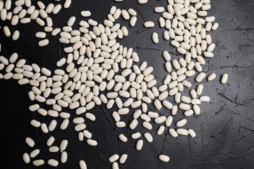 White beans scattered across a textured black surface, showcasing their smooth, glossy appearance...