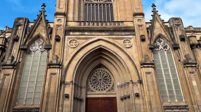 Detail video shot of the portico and main facade of the Cathedral of Mary Immaculate in Vitoria Gasteiz, featuring neo gothic stone architecture, arches and ornamental details under a blue sky. 
