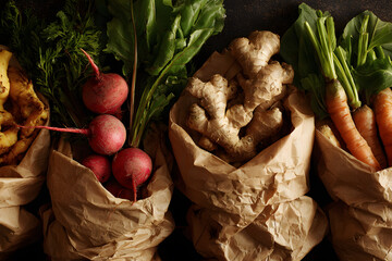 Fresh vegetables in paper bags on a dark surface with roots and greens displayed
