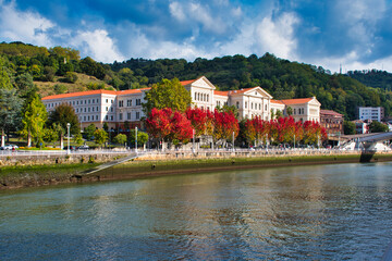 Obraz premium The modern skyline and historic industrial cranes mirrored in the calm, winding waters of the Bilbao river estuary.