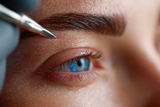 Person receiving precise eyebrow tattooing procedure with a fine tool focusing on enhancing the natural eyebrow shape and definition around the eye area