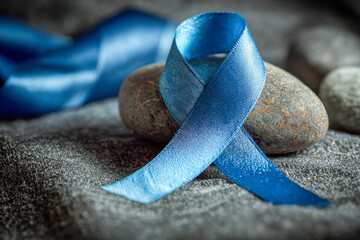 Satin blue awareness ribbon artfully arranged on smooth natural stones with a textured fabric background symbolizing support and health initiatives