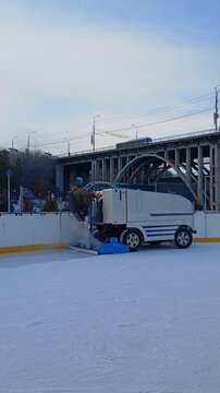 An ice harvester fills the ice at the city skating rink. The ice filling machine drives around the ice rink and renews the ice coating