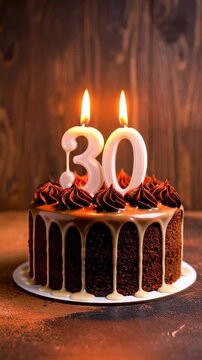 Delicious chocolate cake with caramel drip and lit number 30 candles against a wood panel backdrop for thirtieth celebration