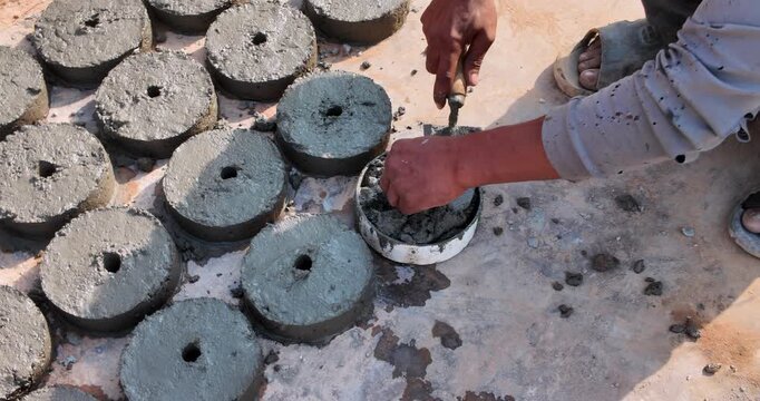 close up of a worker's hands using a trowel to cast circular concrete spacers in molds.