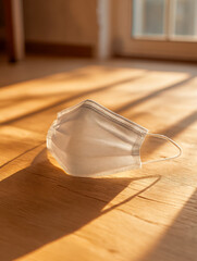 Disposable protective face covering lying on wooden floor illuminated by warm sunlight near window in cozy indoor setting