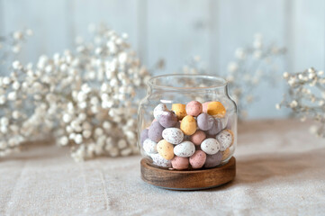 Easter chocolate Multi-Colored eggs in pastel colors in glass jar with gypsophila on background.