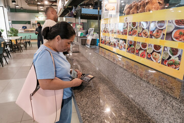 Woman looks at menu in food court while a man stands nearby on a busy day in a public space
