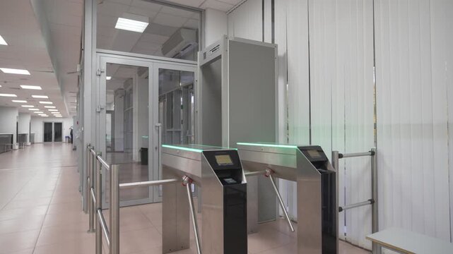 Turnstile stands at entrance of hall with tiled floor and glass doors. Modern design emphasizes security flow along with organized movement