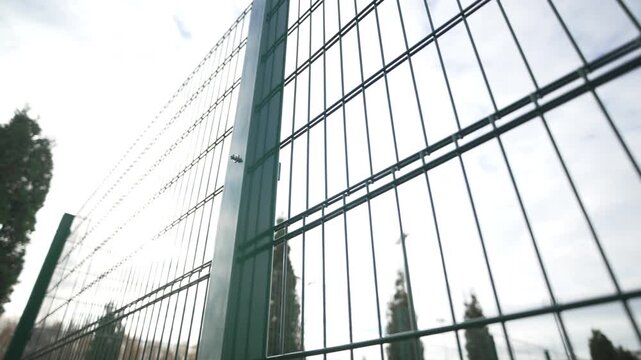 Green mesh fence stretches upward against soft sky with light clouds. Minimal composition emphasizes openness and calm outdoor atmosphere