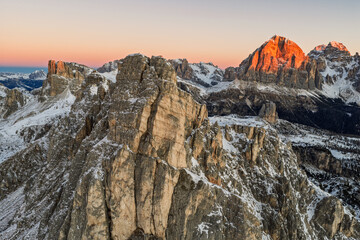Aerial view of a winter sunrise on Giau Pass in Italian Dolomites.Snow covered mountain road. Majestic alpine peaks and warm morning light. Cinque Torri in the Dolomites. Sunrise in winter dolomites