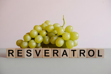 Fresh green grapes beside wooden blocks spelling &ldquo;Resveratrol&rdquo;. Clean studio image highlighting antioxidant-rich fruit