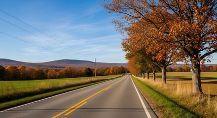 Fototapeta premium Road through autumn landscape with trees and fields under a clear blue sky