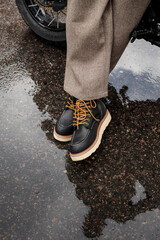 Leather classic boots worn by a man standing on wet asphalt