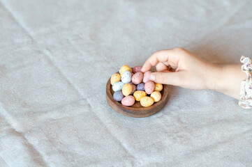 Child hand picking easter chocolate pastel colors eggs from wooden bowl. Top view.