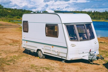 White Caravan Parked by a Scenic Lake with Lush Greenery and Blue Sky