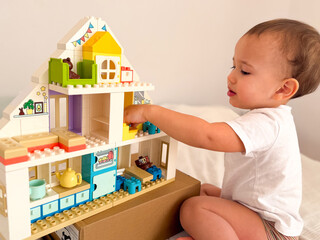 Fototapeta premium Toddler playing with a colorful lego duplo dollhouse