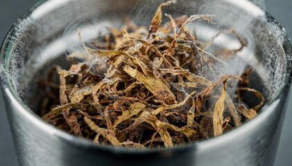 Closeup medium view of tobacco strands coated in a refreshing menthol spray swirling gently in a metallic tumbler for uniform flavor infusion.