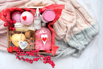 Seasonal gift box idea for Valentine's day, 14 february. cosmetic care set, bath salt, sweets, decor, knitted scarf on marble background. personalized gift basket for family, friends, girl. top view