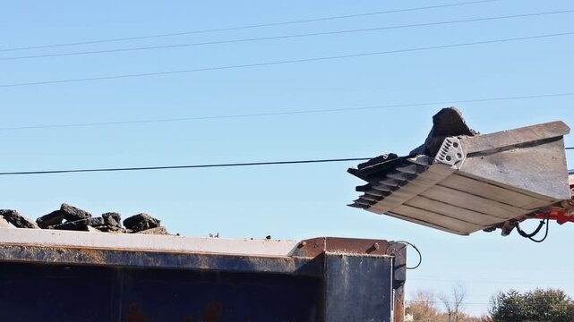 Skid steer machinery unloads soil into truck under construction project.
