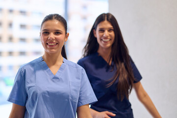 Two healthcare workers share smiles while walking through a hospital corridor during a busy day at work