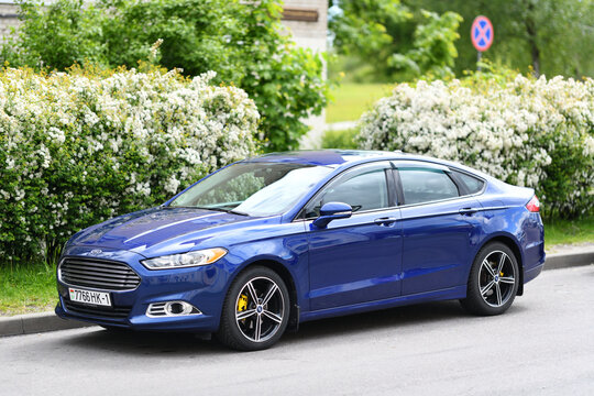 A dynamic blue Ford Fusion sedan (second generation) is parked on the street during the day.