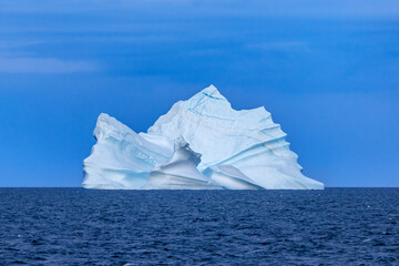 Huge sculptural iceberg with blue seams, against blue sky, in the cold waters of the Arctic Ocean at Bontekoe Island, Northeast Greenland National Park.