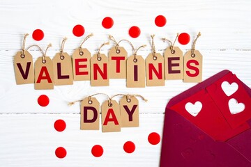 Valentines day greeting card, red envelop with wooden letters on white wooden background with confetti.