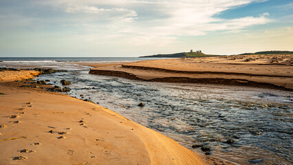 Embleton Burn enters the North Sea in Embleton Bay, which is a long stretch of sand overlooked by the dramatic ruins of Dunstanburgh Castle located on the North Sea coast in the National Landscape