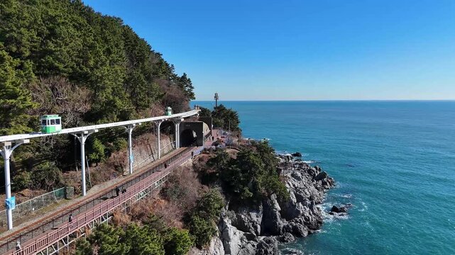 Busan, South Korea, January 2, 2026. The Haeundae Sky Capsule moves along the coast at Haeundae Blueline Park. Tourists walk on the seaside path near one of the most popular attractions in Busan.