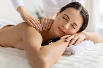 Obraz premium Woman enjoying professional spa massage, resting comfortably with eyes closed. Wellness, beauty treatment, stress relief, and calm atmosphere in bright spa setting
