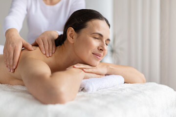 Professional spa massage treatment with female client resting comfortably on massage table, clean bright interior highlighting wellbeing, beauty care, and holistic relaxation