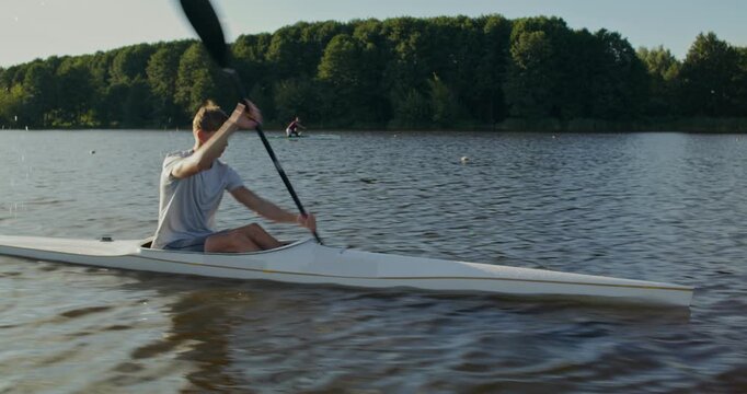 A guy rower in a kayak quickly works with an oar. Men in a kayak and canoe train technique and pace, confidently paddling along the river.
