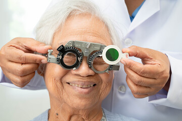 Asian senior woman wearing ophthalmic vision eye test and using optical trial frame.