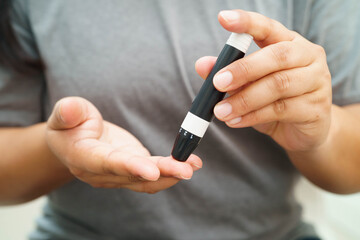 Asian woman self testing to check blood sugar level diabetes by digital lancet on finger at home.