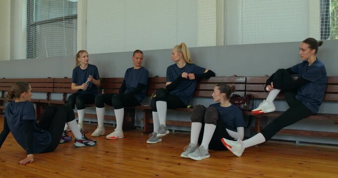 The volleyball players chat after the game and drink water. The volleyball team rests after the game.