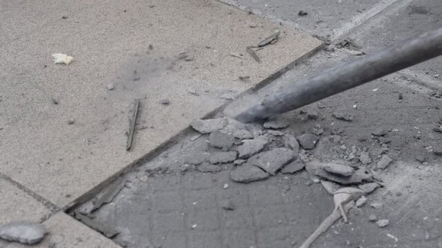 Removing a concrete floor with a hand hammer. Concrete rubble on the construction site of a house. Destruction of old tiles. Male construction removes the old tile from the floor with a hammer drill.
