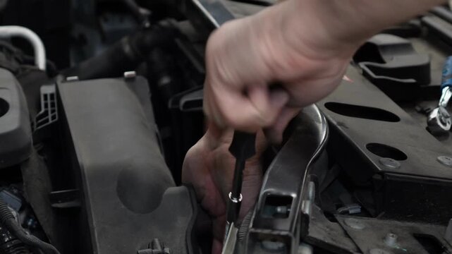 Close up of a mechanic hand repairing a car engine compartment with a socket wrench tool inside a vehicle service station workshop.
