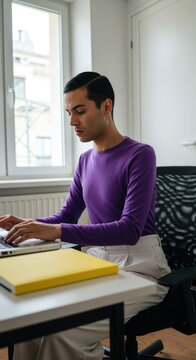 Non-binary person working on laptop at desk. Diversity and inclusion concept. Business concept. Workplace environment. Young latin person using computer.