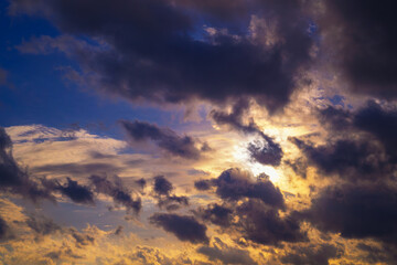 Abstract background with a picturesque cloudy landscape featuring smoky dark textures of clouds in the rays of the yellow setting sun.