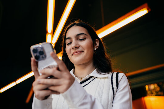 Woman smiling while reading something on smartphone screen, emphasizing satisfaction and ease of digital interaction in modern tech culture.