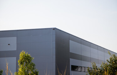 Modern industrial warehouse roof with white corrugated metal sheet against blue sky.Exterior of modern gray industrial building or logistics center with green trees