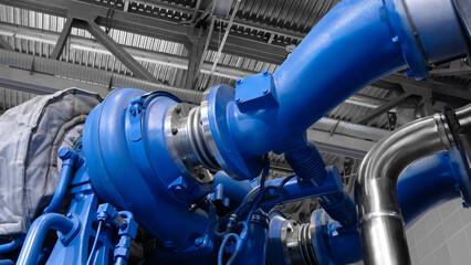 Large  piston gas engine electric generator with many valves and pipes. The engine is orange and...