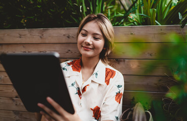 Smiling young woman using digital tablet with stylus in outdoor setting, engaging in modern creative work surrounded by plants, highlighting harmony between nature and technology. © BullRun