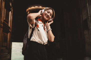 Portrait of smiling young Asian woman enjoying sound in wireless headphones, gently adjusting earcups, radiating relaxed confidence and love for modern digital experiences.