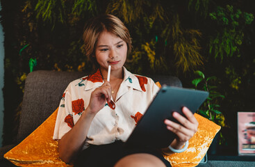 Asian woman holding tablet and stylus, thinking with focus, concept of freelance creativity, online...