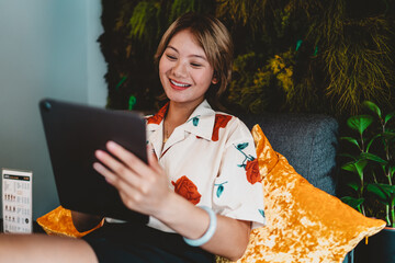 Asian woman smiling with tablet in hand, symbolizing freelance adaptability, digital communication, and positive engagement with online creativity. © BullRun