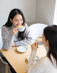 Two young Asian women drinking coffee in cafe. They are talking and smiling.