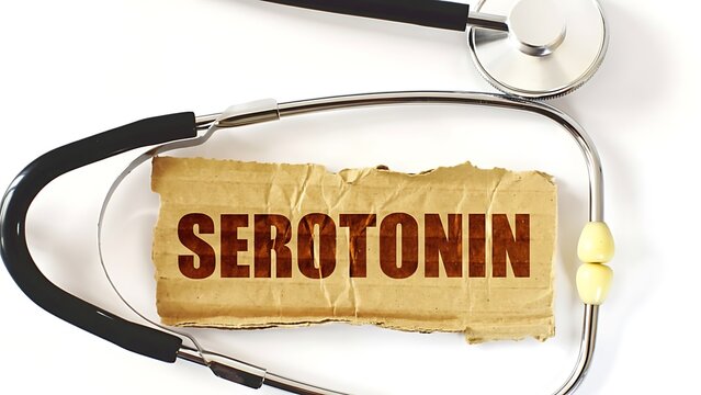 Stethoscope medical symbol resting on torn cardboard piece with the word Serotonin written in bold brown letters on white background