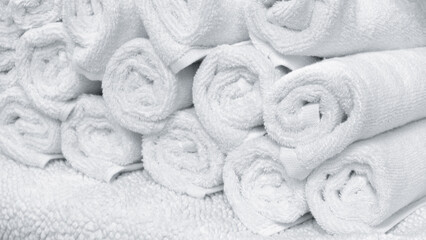 A stack of white towels on a white surface. The towels are rolled up and stacked on top of each...